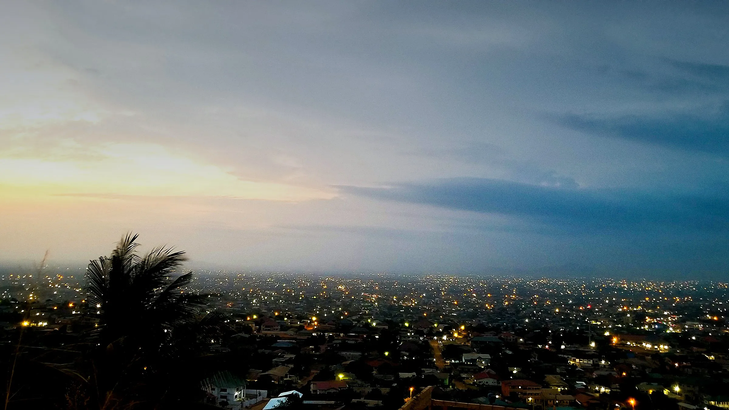 The city of Accra at dusk, its lights coming on beneath a pale evening sky