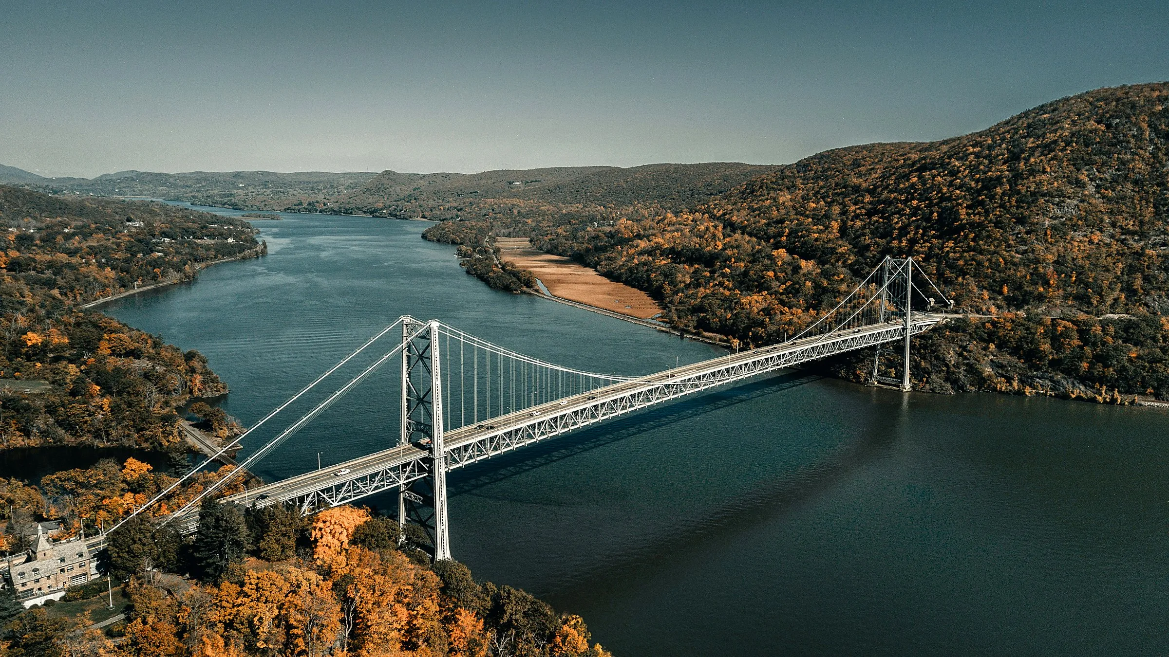 A suspension bridge crossing a wide river between forested hills