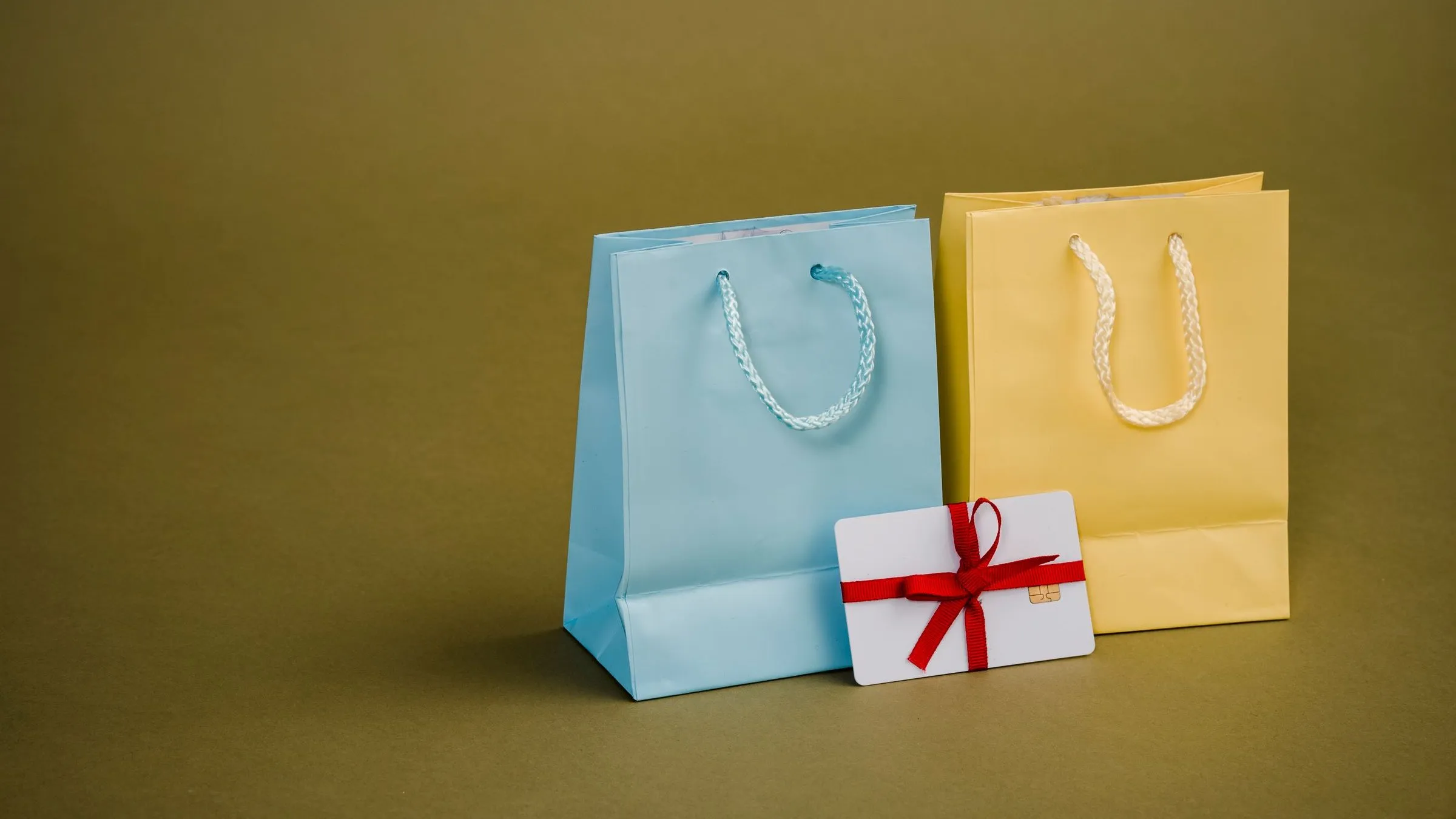 Two paper shopping bags beside a gift card tied with a red ribbon